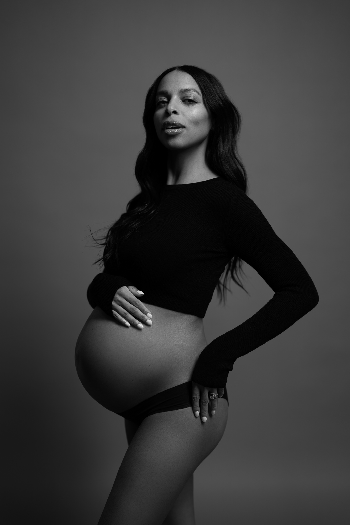 Elegant profile of a pregnant Black woman with one hand on her lower back and one on her belly, posing confidently in a studio.