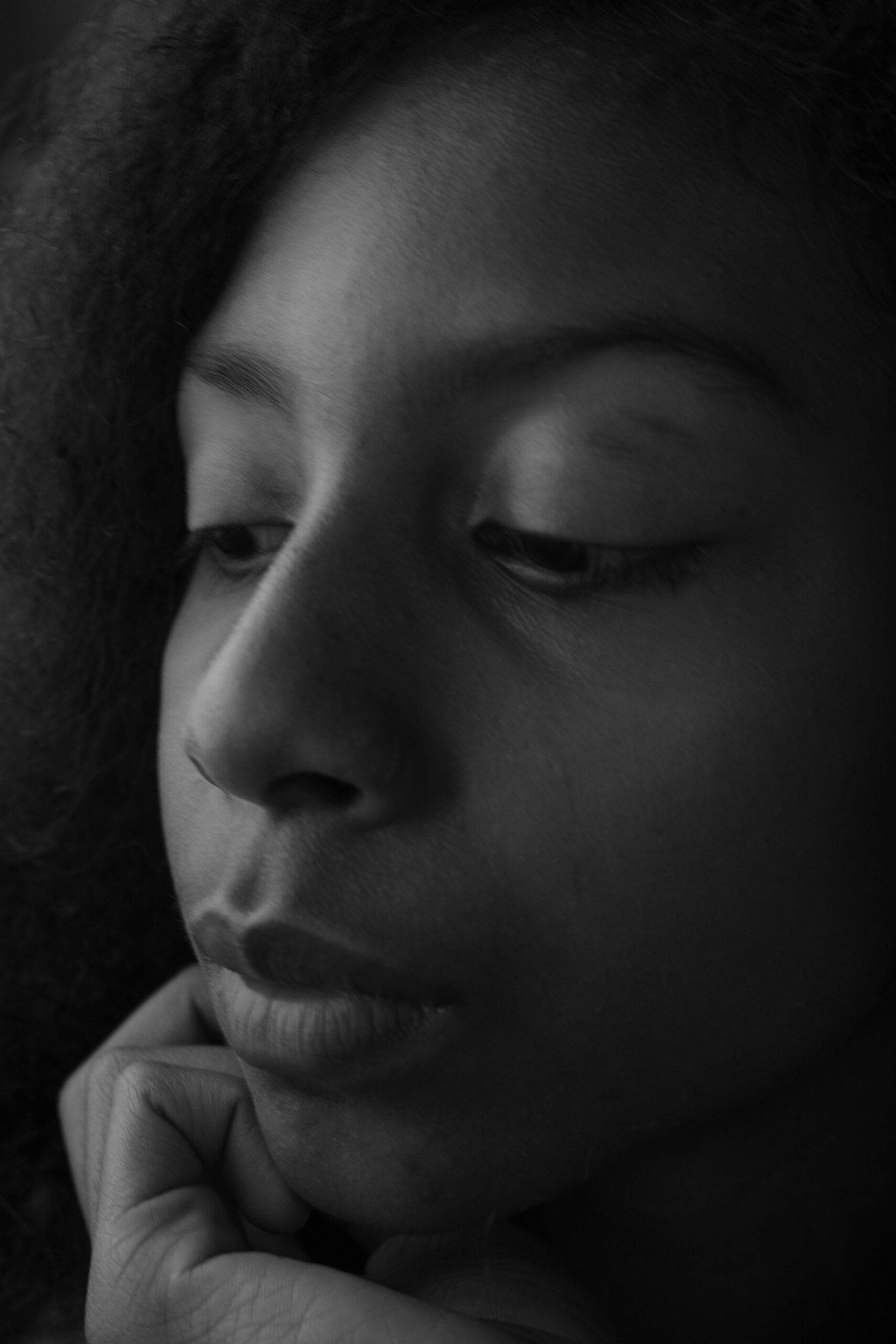 Close-up black-and-white portrait of an 11-year-old girl resting her chin on her hand. Her downcast eyes and soft expression convey a sense of quiet introspection and gentle thoughtfulness, capturing an intimate and reflective moment.