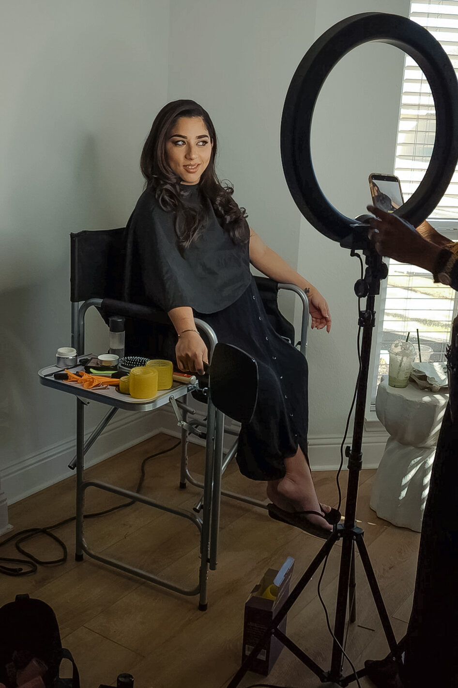 Pregnant client sitting in a makeup chair with soft curls styled, preparing for her studio maternity session at JPF Galleries in Fort Worth