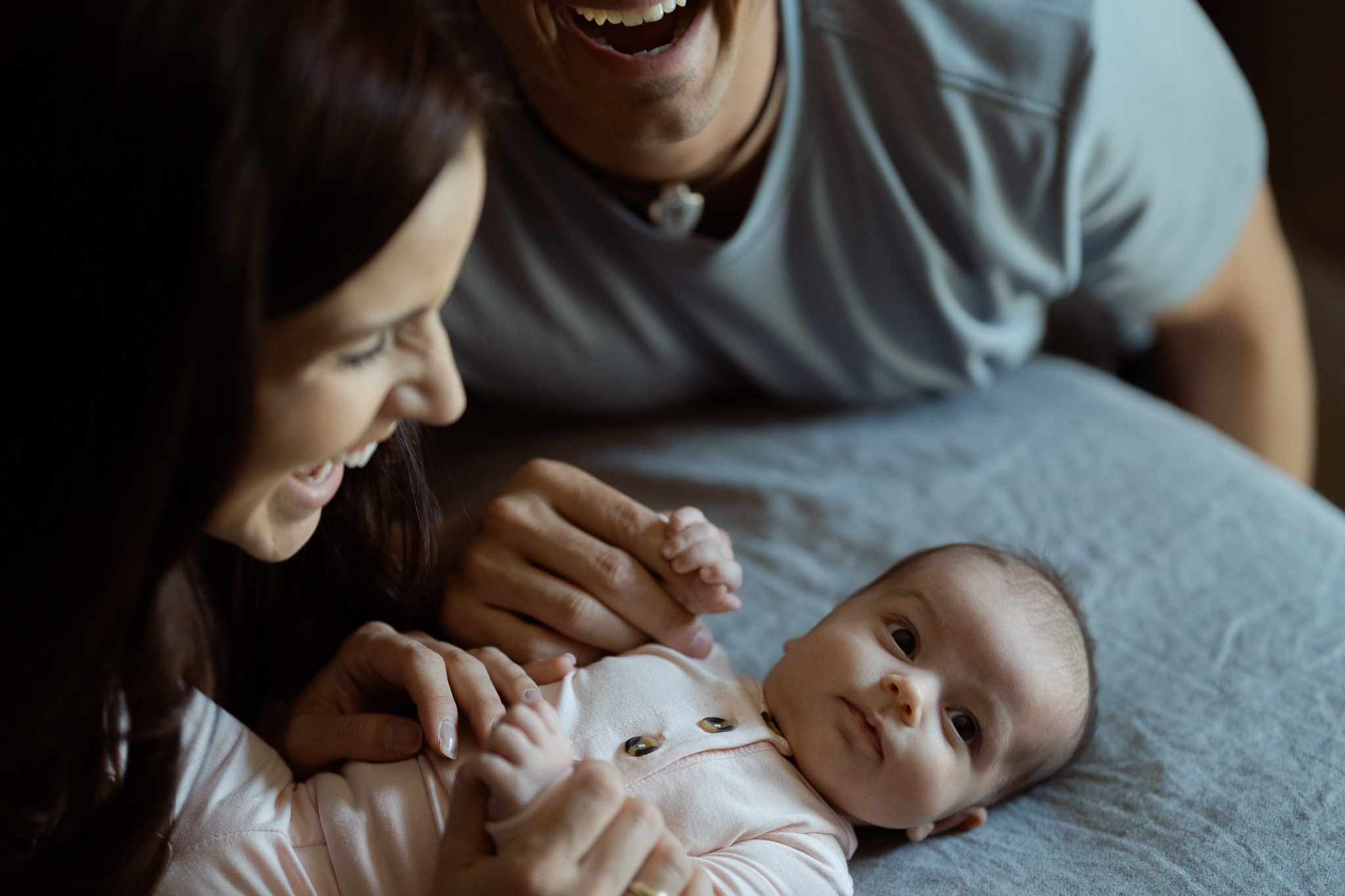 Baby lying on bed while parents share a laugh nearby.