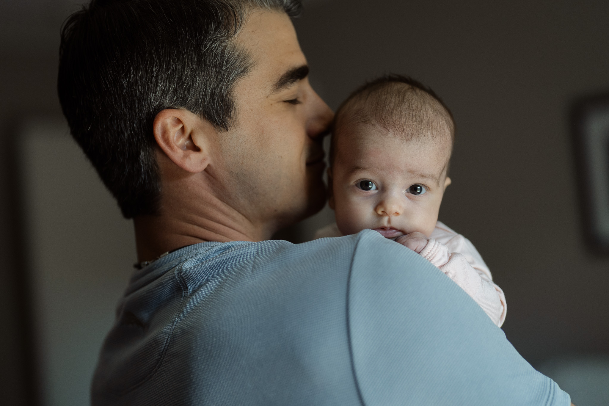 Father holding his newborn in soft window light at home.